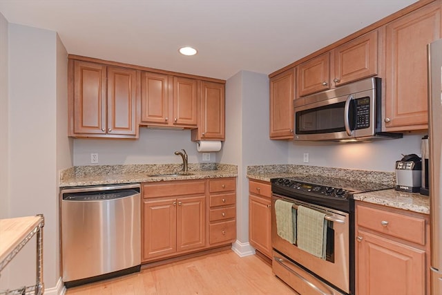 kitchen with appliances with stainless steel finishes, light stone counters, light wood-style floors, a sink, and recessed lighting