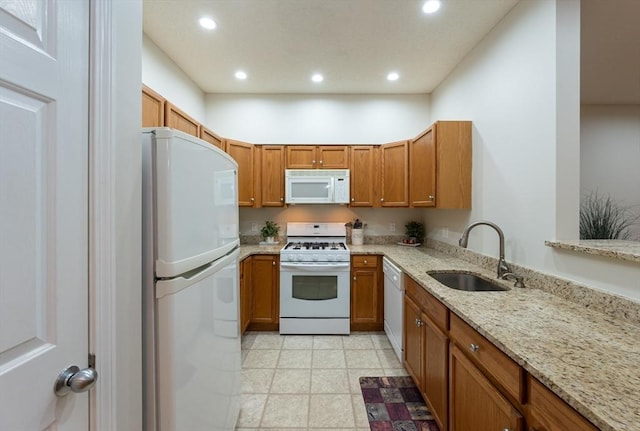 kitchen with white appliances, a sink, recessed lighting, light stone counters, and brown cabinets