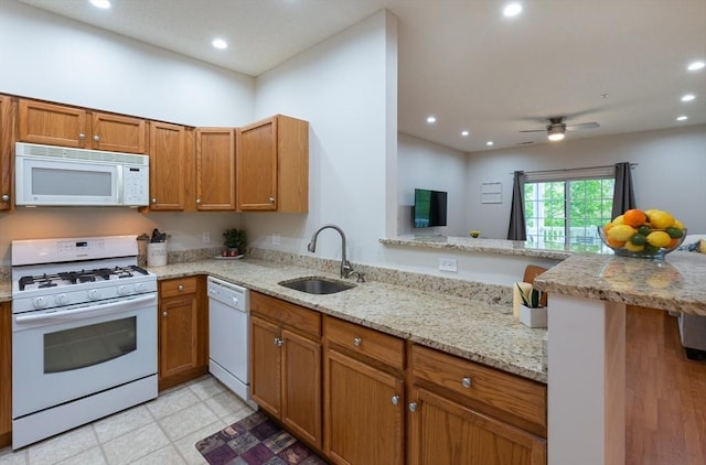 kitchen featuring white appliances, a sink, recessed lighting, light stone counters, and a peninsula