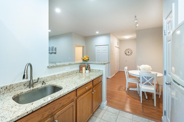 kitchen featuring a sink, brown cabinetry, light stone counters, recessed lighting, and a peninsula