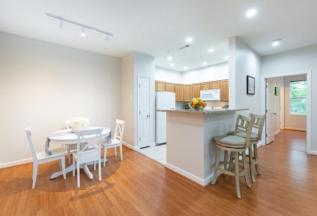 kitchen with white appliances, rail lighting, light wood-style flooring, a kitchen breakfast bar, and baseboards