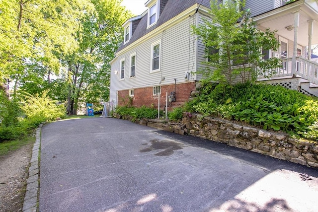 view of property exterior featuring mansard roof, brick siding, and driveway