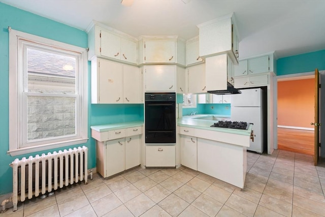 kitchen featuring white cabinets, white refrigerator, light tile patterned flooring, and radiator heating unit