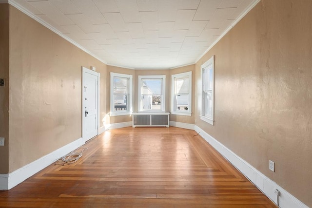 spare room featuring hardwood / wood-style floors, radiator heating unit, and crown molding