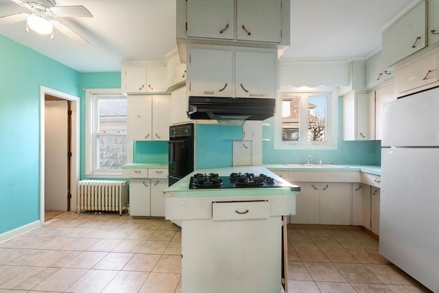 kitchen featuring sink, black oven, white fridge, radiator heating unit, and stainless steel gas cooktop