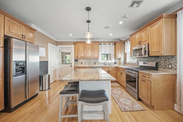 kitchen with crown molding, a center island, hanging light fixtures, stainless steel appliances, and light stone countertops