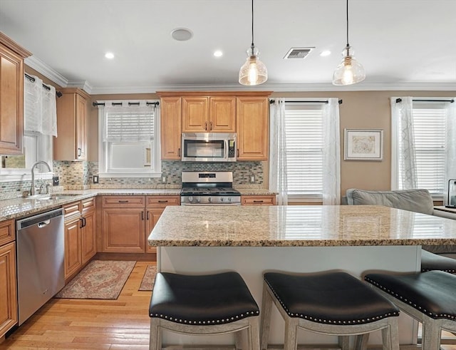 kitchen featuring a kitchen island, appliances with stainless steel finishes, pendant lighting, sink, and ornamental molding