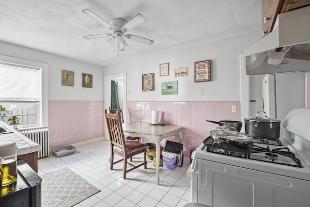 tiled dining space with ceiling fan, radiator, and tile walls