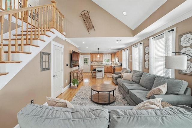 living room with crown molding, high vaulted ceiling, and light hardwood / wood-style flooring