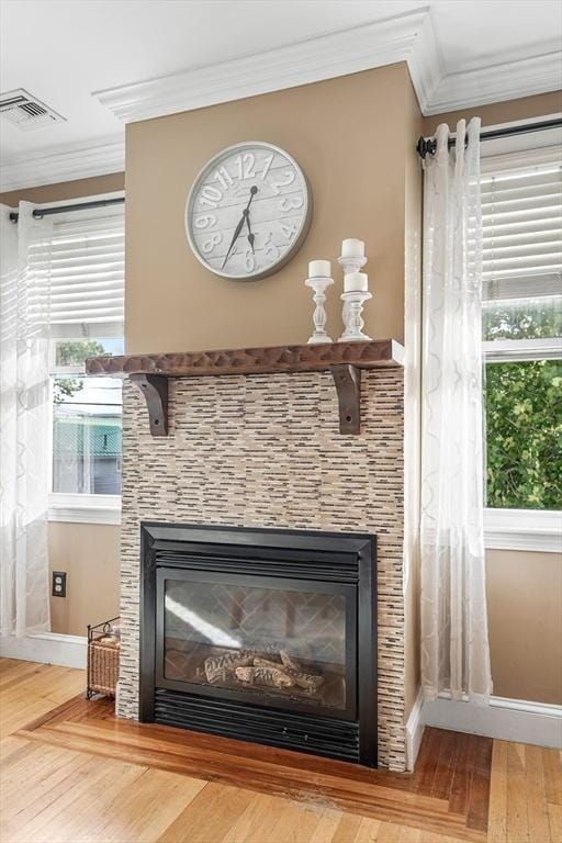 room details featuring a tiled fireplace, crown molding, and wood-type flooring