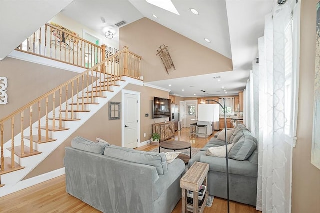 living room with crown molding, high vaulted ceiling, light wood-type flooring, and a skylight