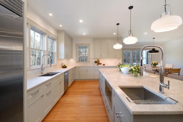 kitchen featuring decorative light fixtures, light hardwood / wood-style floors, sink, and appliances with stainless steel finishes