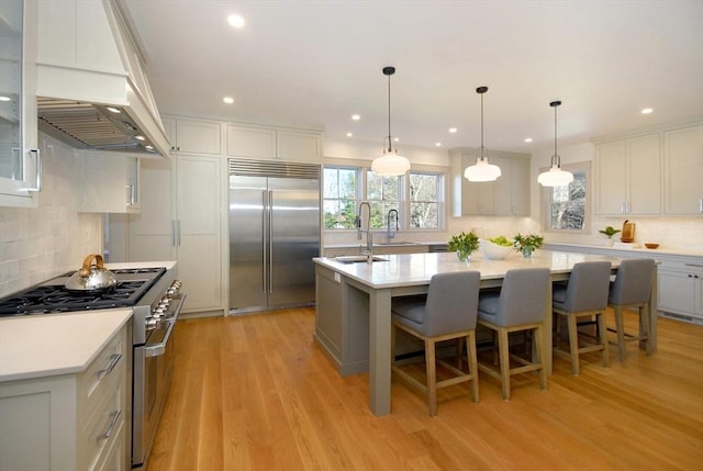 kitchen featuring custom exhaust hood, sink, light hardwood / wood-style flooring, high quality appliances, and an island with sink