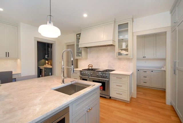 kitchen with double oven range, sink, light hardwood / wood-style flooring, decorative light fixtures, and custom range hood