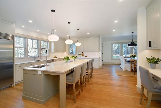 kitchen featuring decorative light fixtures, light wood-type flooring, a center island with sink, and stainless steel built in fridge