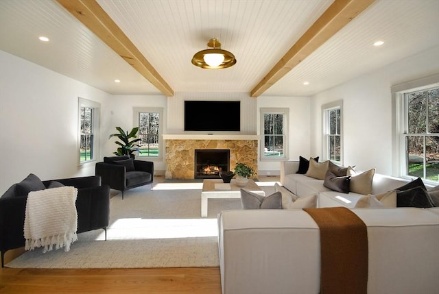 living room with a stone fireplace, light hardwood / wood-style flooring, and beamed ceiling