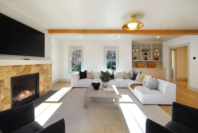 living room with a stone fireplace, light hardwood / wood-style flooring, and beamed ceiling