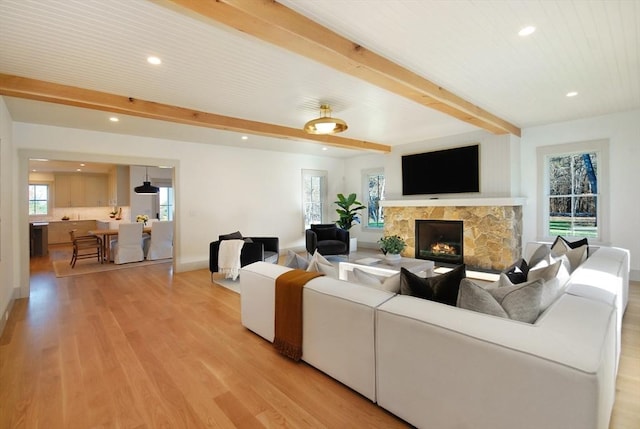 living room with beam ceiling, a stone fireplace, and light wood-type flooring