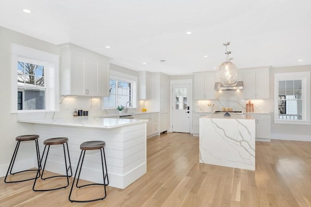 kitchen with white cabinetry, a center island, light stone counters, pendant lighting, and light hardwood / wood-style floors