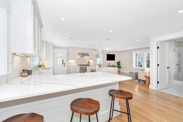 kitchen with a kitchen breakfast bar, white cabinetry, light stone counters, and kitchen peninsula