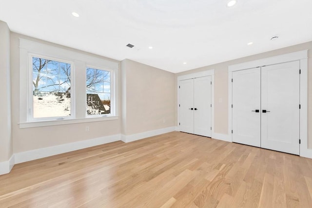 unfurnished bedroom with light wood-type flooring and two closets