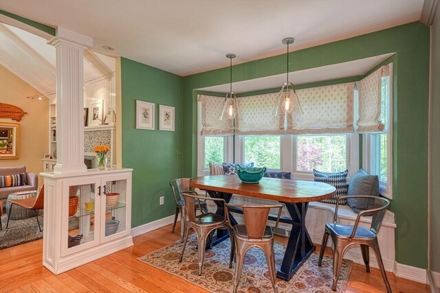 dining space featuring ornate columns, healthy amount of natural light, light wood-style flooring, and lofted ceiling