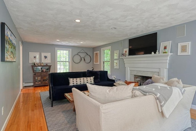 living area with a baseboard radiator, light wood-style flooring, a premium fireplace, recessed lighting, and baseboards