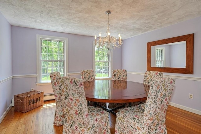 dining room with baseboard heating, wood-type flooring, a textured ceiling, a chandelier, and baseboards