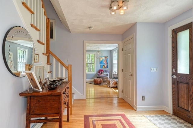 foyer entrance with light wood finished floors, a textured ceiling, stairs, and baseboards