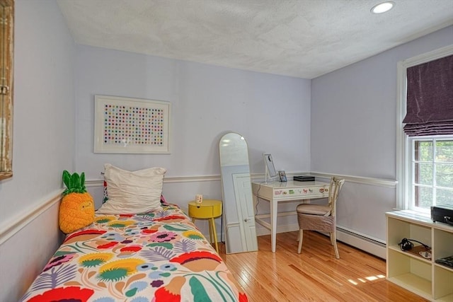 bedroom with a baseboard radiator, wood finished floors, a textured ceiling, and recessed lighting