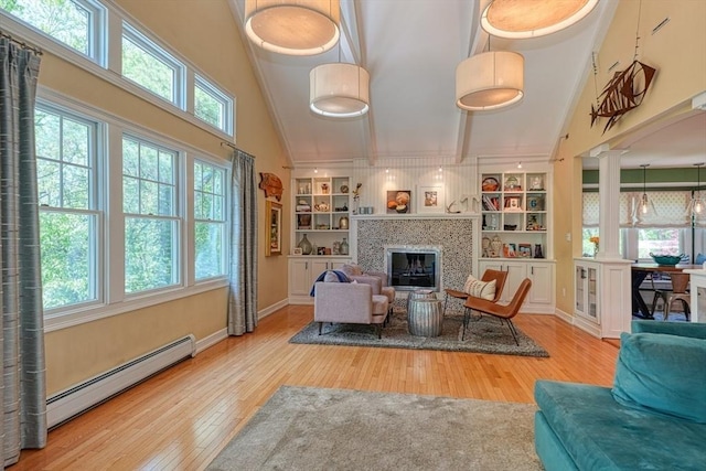living room with baseboard heating, decorative columns, plenty of natural light, wood finished floors, and a towering ceiling