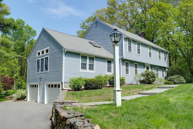 view of front facade featuring an attached garage, a chimney, asphalt driveway, and a front lawn