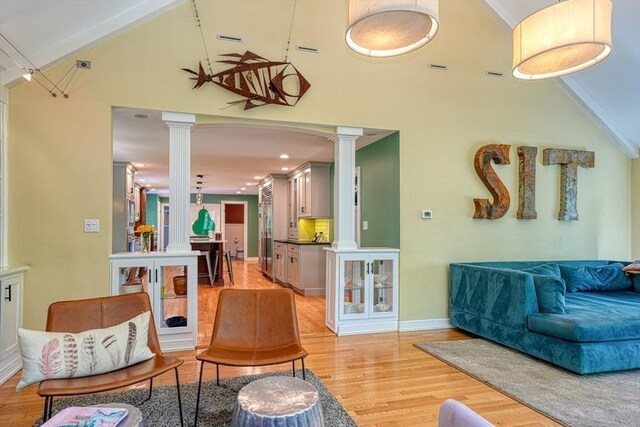 living room with decorative columns, high vaulted ceiling, light wood-style floors, and baseboards