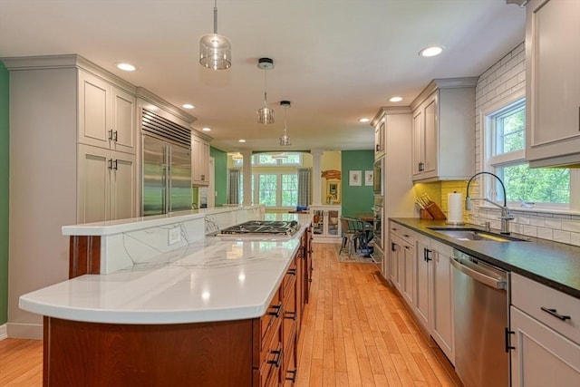 kitchen featuring built in appliances, a sink, a kitchen island, light wood-type flooring, and backsplash