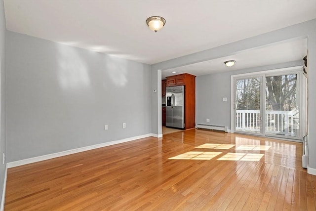 unfurnished room with baseboard heating, baseboards, and light wood-style floors