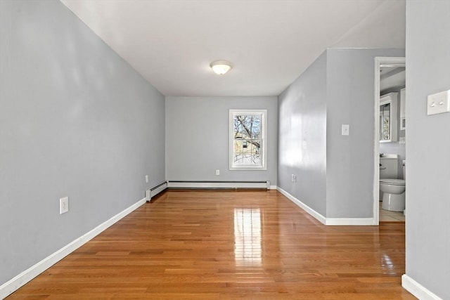 empty room with wood finished floors, baseboards, and baseboard heating