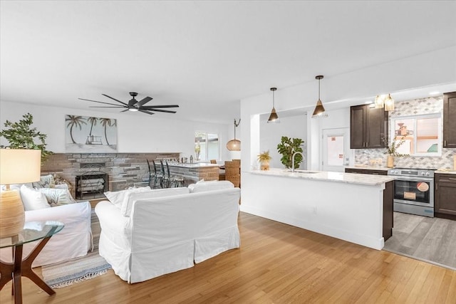 living room featuring ceiling fan, a stone fireplace, sink, and light wood-type flooring