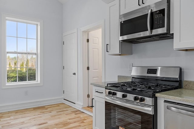 kitchen with baseboards, light wood finished floors, white cabinetry, and stainless steel appliances