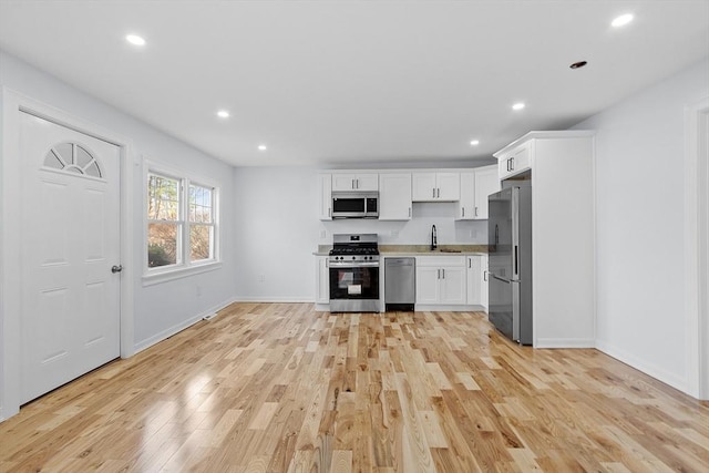 kitchen with baseboards, white cabinetry, a sink, light wood-style flooring, and appliances with stainless steel finishes