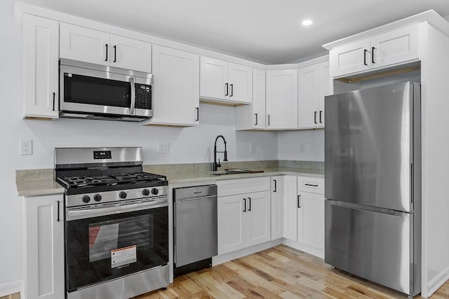 kitchen featuring light stone counters, appliances with stainless steel finishes, a sink, light wood-style floors, and white cabinetry