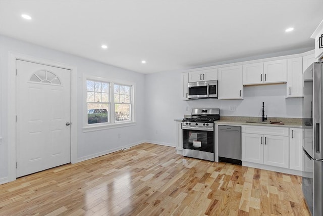 kitchen featuring white cabinets, appliances with stainless steel finishes, a sink, light wood-style floors, and baseboards