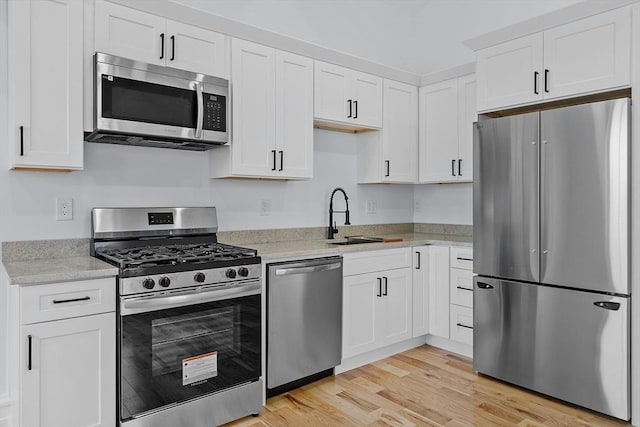 kitchen with white cabinets, appliances with stainless steel finishes, light stone counters, a sink, and light wood-style flooring