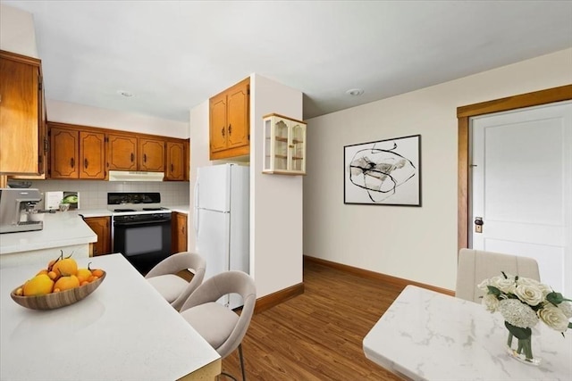kitchen featuring light countertops, wood finished floors, brown cabinets, under cabinet range hood, and white appliances
