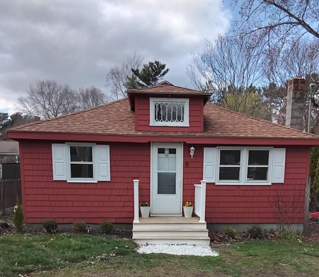 view of front of house with a front yard, roof with shingles, and a chimney