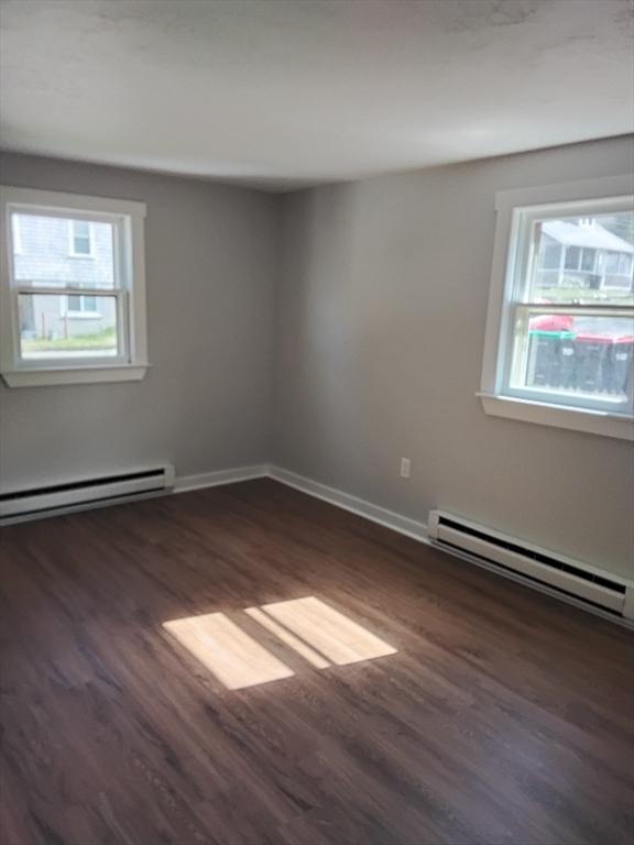 spare room featuring dark wood-type flooring, plenty of natural light, and baseboard heating