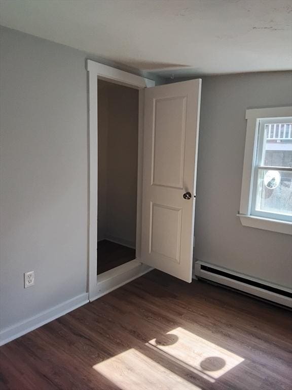 unfurnished bedroom featuring dark wood-type flooring, a baseboard radiator, and baseboards