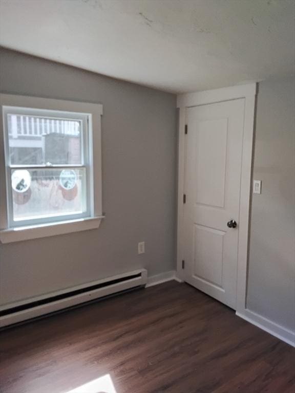 empty room featuring dark wood-type flooring, a baseboard radiator, and baseboards