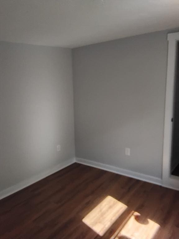 spare room featuring baseboards and dark wood finished floors