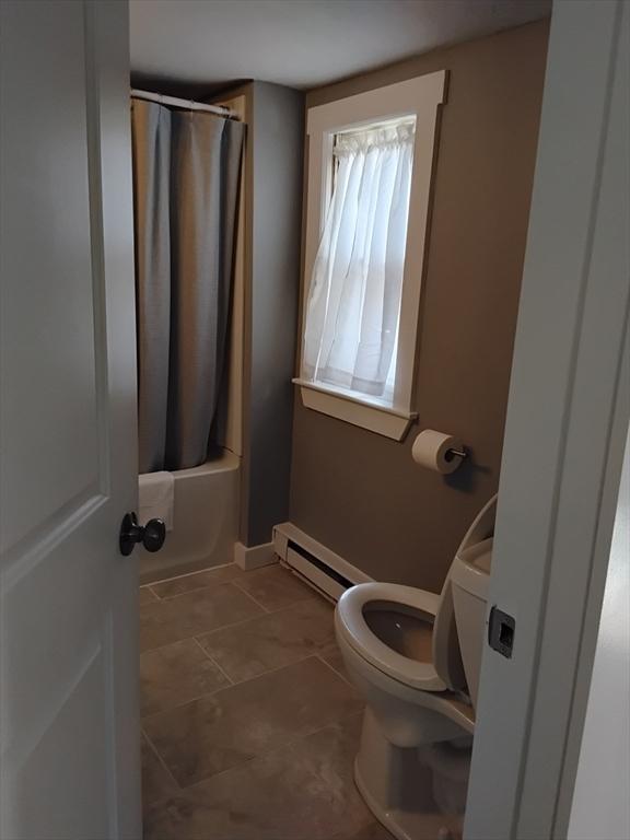 bathroom featuring toilet, a baseboard heating unit, tile patterned flooring, and shower / tub combo with curtain
