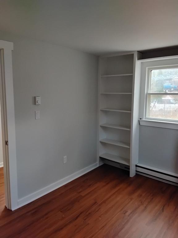 unfurnished bedroom featuring a baseboard heating unit, dark wood-style flooring, and baseboards
